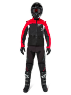 Motocross-kører iført komplet off-road-udstyr, Alpinestars Pro-Dura jakke i sort, lys rød og hvid, sorte bukser med røde detaljer, sort hjelm med røde goggles, sort-hvide støvler, koordineret sæt til enduro- og trailkørsel