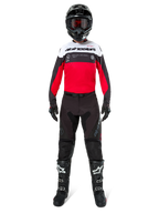 Motocross-kører iført Alpinestars Pro-Dura bukser i sort og magnet, kombineret med en rød, hvid og sort trøje, sort hjelm og sorte støvler, komplet off-road racing-udstyr, holdbart og letvægtsdesign til enduro-kørsel