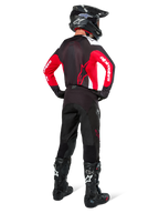 Alpinestars Pro-Dura bukser i Black Magnet White, motocrossrytter set bagfra, kombineret med rød og sort trøje og sorte støvler, koordineret off-road udstyrssæt til enduro-kørsel