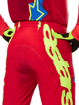 Alpinestars 2025 Supertech Maker Pants, Motocross Pants, Bright Red and Yellow Fluo, rear close-up showing bold neon yellow graphics, worn with matching red jersey and yellow/black gloves
