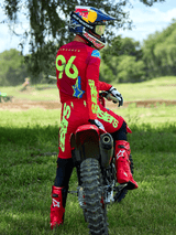 Motocross rider sitting on a red dirt bike, Alpinestars 2025 Supertech Maker Pants in Bright Red and Yellow Fluo, matching red jersey with '96' and 'LAWRENCE' on the back, red racing boots, and a Red Bull branded helmet, professional off-road racing gear set