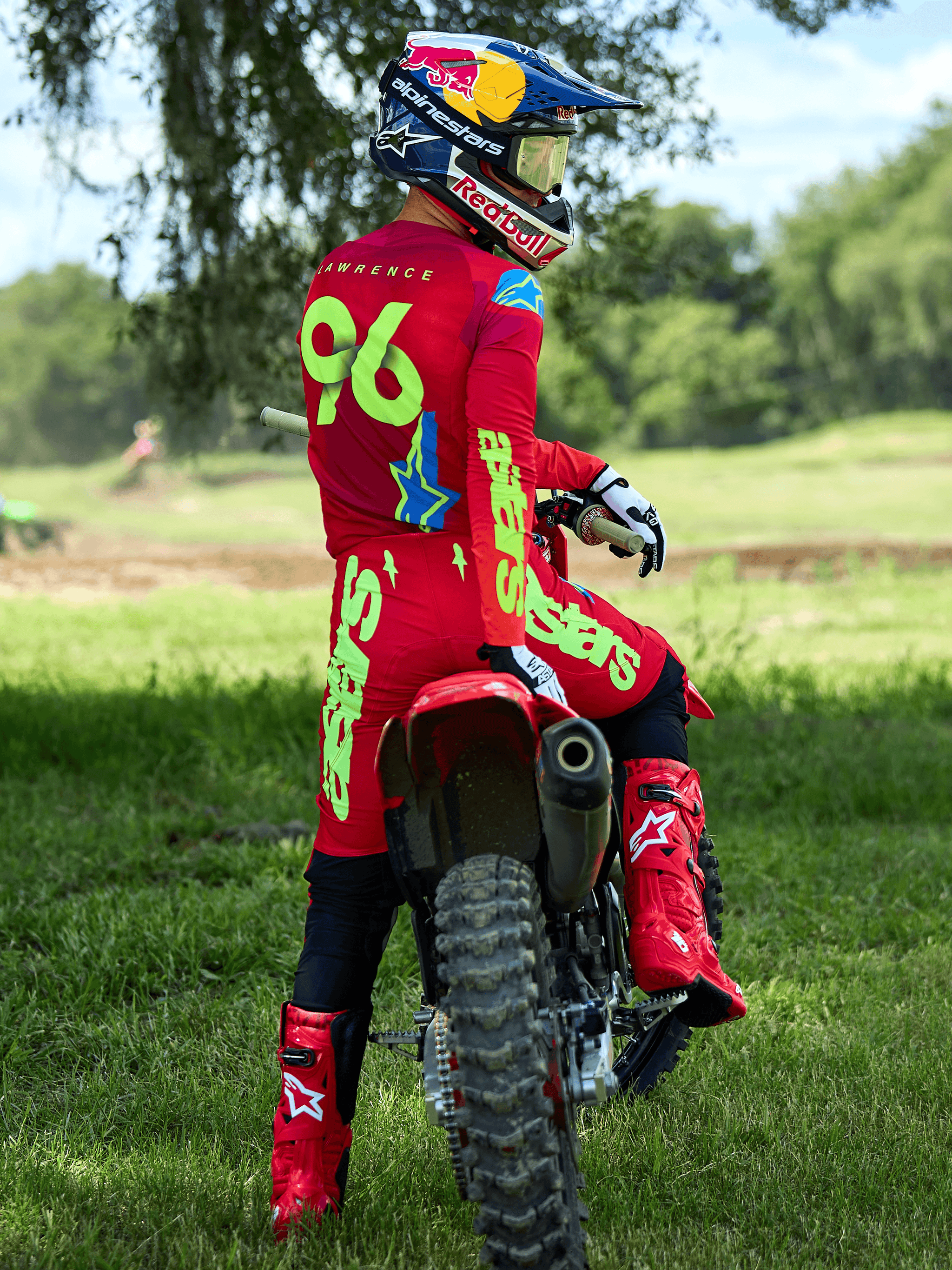 Motocross rider sitting on a red dirt bike, Alpinestars 2025 Supertech Maker Pants in Bright Red and Yellow Fluo, matching red jersey with '96' and 'LAWRENCE' on the back, red racing boots, and a Red Bull branded helmet, professional off-road racing gear set