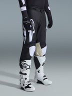 Alpinestars 2026 Racer Air Riway bukser, motocrossbukser, sort og hvid, vist med hvide og sorte Tech Series-støvler og sort langærmet trøje, med hvid Alpinestars-branding, laserskårne perforationer og indvendige knæpaneler i lysebrunt gedelæder til off-road kørsel.