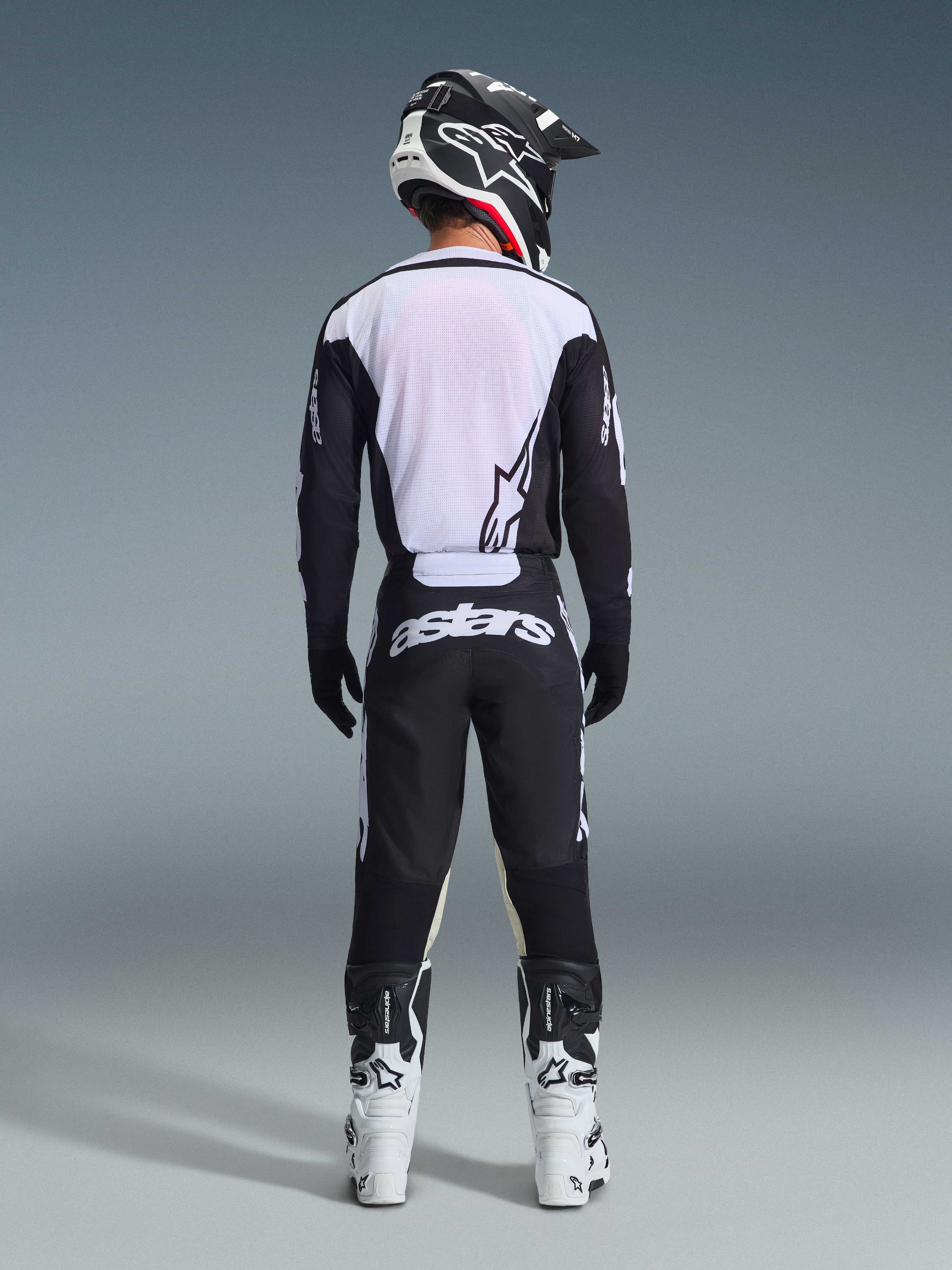 Alpinestars 2026 Racer Air Riway bukser, set bagfra, sort og hvid, matchende sort og hvid langærmet jersey, hvide og sorte racingstøvler og sort hjelm med Alpinestars-branding, motocross-udstyr