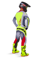 Alpinestars 2025 Techstar Melt Gear Set, motocross-kører set bagfra, grå jersey med neongult rygpanel og rødt stjernelogo, grå og røde bukser med tydelig neongul 'Alpinestars'-branding hen over bagen, klare neongule motocross-støvler og matchende hjelm.