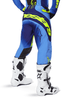 Alpinestars 2025 Techstar Melt Pants, Motocross Pants, Yellow Fluo Blue, rear view featuring large yellow branding across the seat and dark blue accents, worn with white Alpinestars Tech 10 boots and a matching jersey.