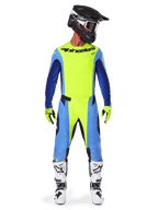 Motocrosskører iført Alpinestars 2025 Techstar Melt-udstyrssæt, neongul jersey med blå og navyblå ærmer, matchende gule og blå bukser, sort og hvid hjelm med goggles, hvide og sorte støvler, gule og sorte handsker, koordineret outfit til off-road racing