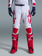 Alpinestars 2026 Racer Riway bukser, motocross-bukser, hvid, blå og rød, båret med røde støvler og mørkeblå handsker, med store røde logoer på lårene og røde knæpaneler, sportsligt forbuet design med justerbart taljespænde