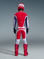 Motocrosskører set bagfra iført fuldt racerudstyr, Alpinestars 2026 Racer Riway-bukser i hvid, blå og rød med matchende trøje, røde støvler og hjelm, stort 'astars'-logo på sædet, koordineret motocross-sæt