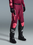 Alpinestars 2026 Racer Riway bukser, motocrossbukser, Dark Red Coral, med store lyserøde stjernelogoer og sorte indvendige knæpaneler, båret med sorte motocrossstøvler og sorte handsker, atletisk racerpasform til off-road kørsel