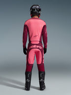 Set bagfra af en motocross-kører iført 2026 Racer Riway-udstyrssættet, lyserød og bordeauxrød jersey, matchende bordeauxrøde bukser med lyserødt 'astars'-logo bagpå, sort hjelm, sorte støvler og sorte handsker, koordineret outfit til terrænkørsel