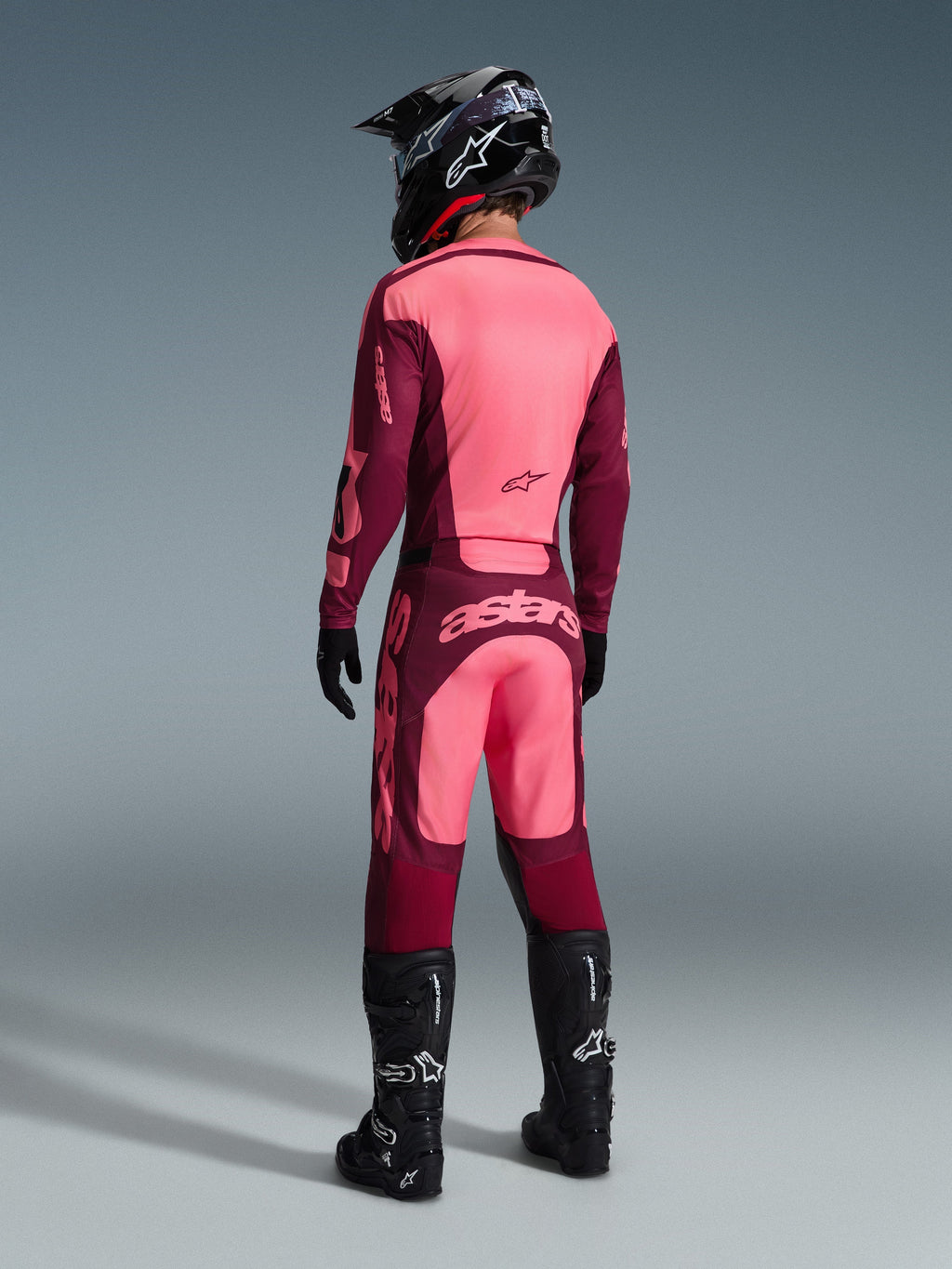 Alpinestars 2026 Racer Riway bukser, motocrossbukser, Dark Red Coral, set bagfra på en kører iført en matchende trøje, sort hjelm og sorte støvler, med markant koralfarvet branding på sædet og ergonomisk atletisk pasform til off-road racing