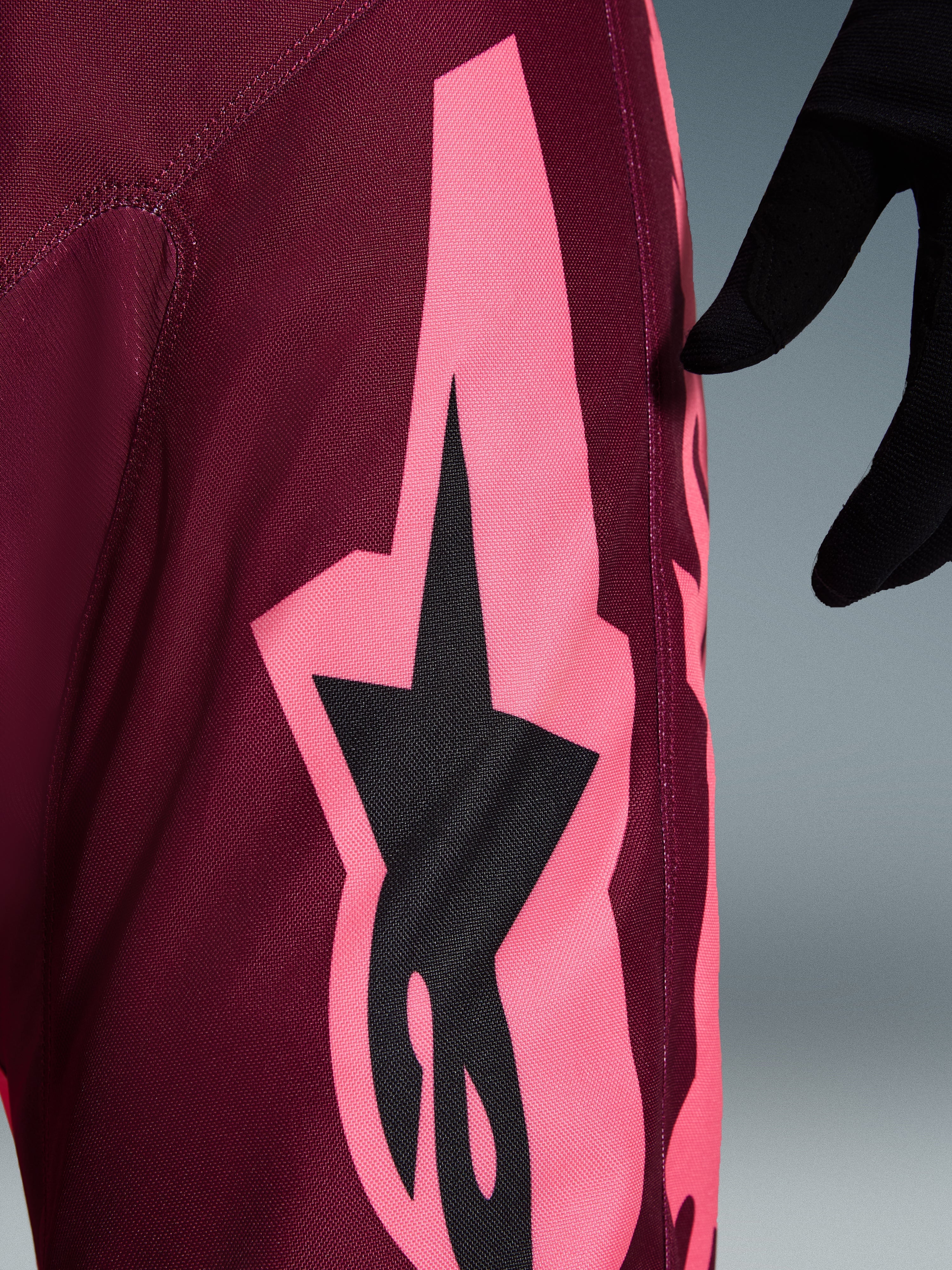 Alpinestars 2026 Racer Riway bukser, motocross-bukser, Dark Red Coral, nærbillede der viser en stor koralrosa vinklet grafik og sort stjernelogo, der fremhæver den slidstærke polyfabric-tekstur og performance-syninger