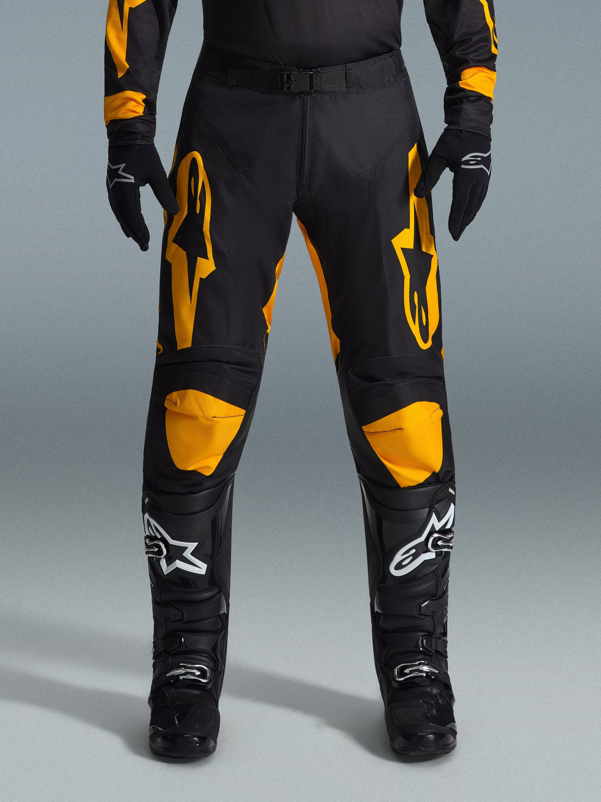 Alpinestars 2026 Racer Riway bukser, motocrossbukser, gul og sort, bæres med sorte motocrosshandsker og sorte støvler med hvide logoer, med store gule Alpinestars-logoer på lårene og gule knæpaneler, holdbart design til off-road racerpræstation