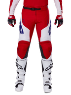 Alpinestars 2025 Racer Veil Pants, Motocross Pants, Bright Red and White, worn with matching red gloves and white boots, featuring blue branding on the thighs and a black waist belt, ergonomic sport cut for performance riding