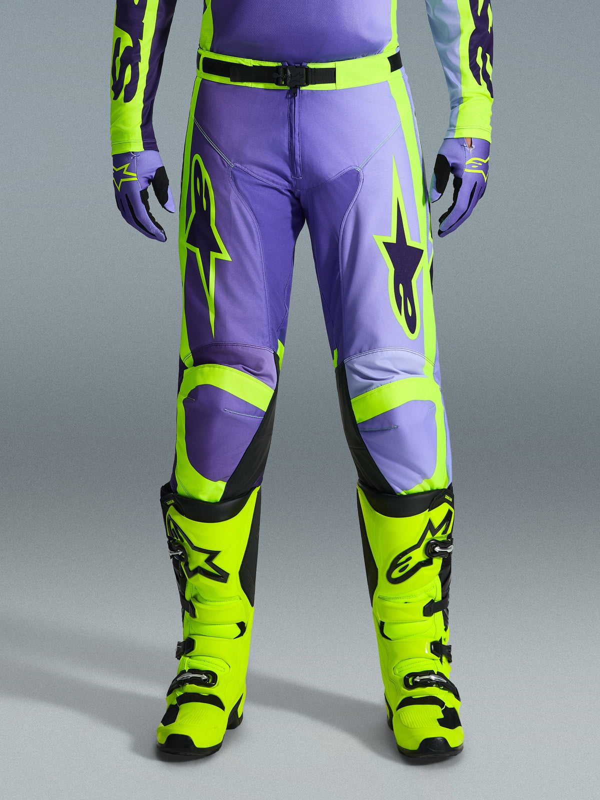 Alpinestars 2026 Racer Portl bukser, motocross-bukser, lilla og neongul, båret med matchende neongule støvler og lilla handsker, med store stjernelogoer og holdbar polyfabric-konstruktion til off-road racing