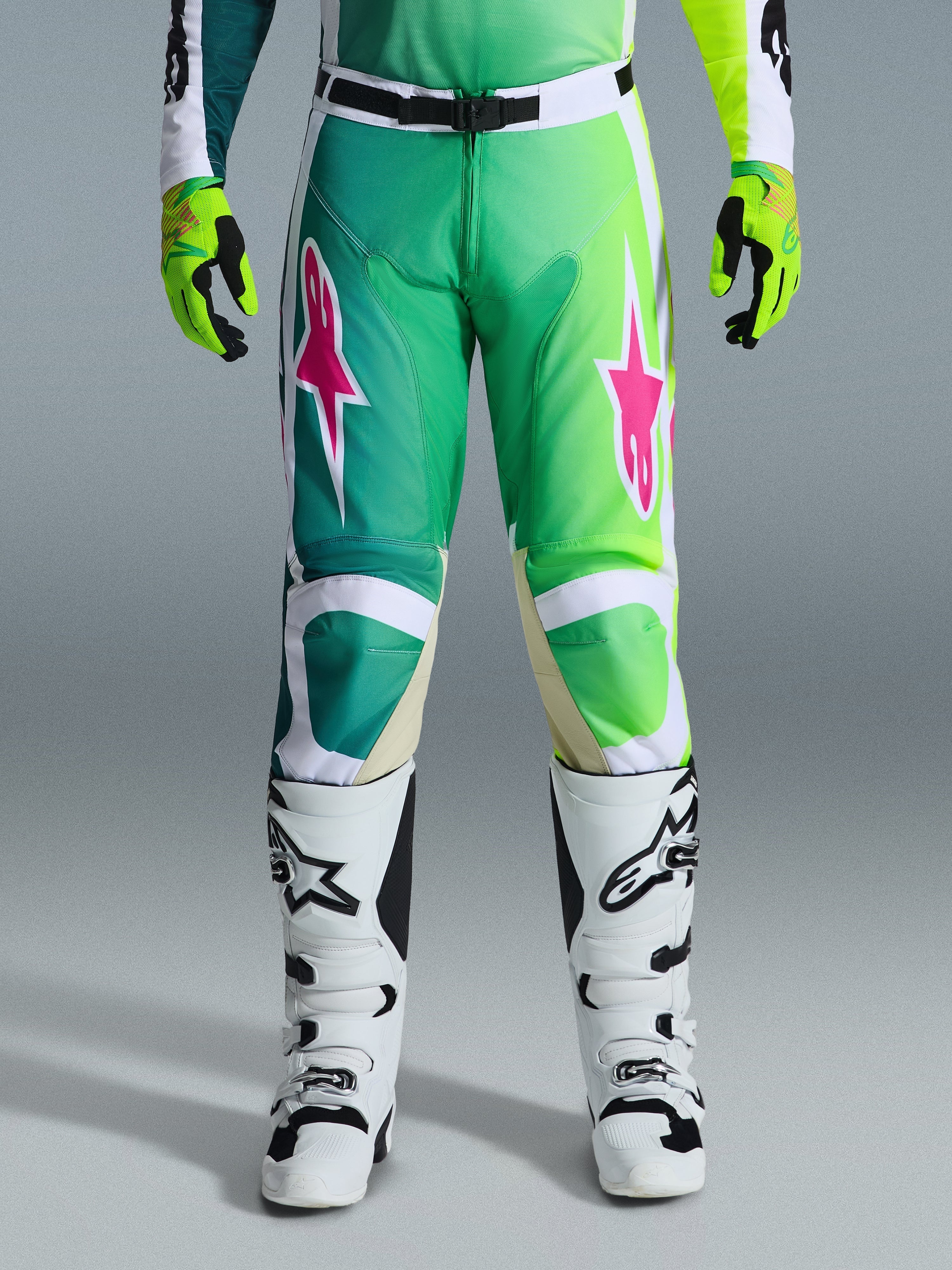 Alpinestars 2026 Racer Portl bukser, motocross-bukser, grøn, hvid og sort med lyserøde stjerne-logoer, båret med hvide og sorte støvler og limegrønne handsker, med gradient-design og ergonomisk pasform til terrænkørsel