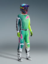 Motocross rider wearing Alpinestars 2026 Racer Portl Pants and matching jersey in Green, White, and Black with pink logo accents, colorful helmet, white and black racing boots, and neon green gloves, complete gear set for off-road racing
