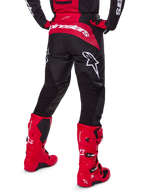 Alpinestars 2025 Fluid Haul-udstyrssæt, set bagfra, sorte og røde motocrossbukser med store hvide logoer, matchende trøje og røde Tech 7-støvler, koordineret off-road racingudstyr