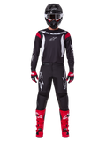 Alpinestars 2025 Fluid Haul-udstyrssæt, motocross-kører i komplet racerudstyr, sort jersey med røde skulderdetaljer og hvide logoer, sorte bukser med hvidt stjerne-branding, klare røde støvler, røde og sorte handsker, sort hjelm med hvide beskyttelsesbriller, koordineret off-road performance-look