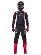 Alpinestars 2025 Fluid Haul-udstyrssæt, motocross-kører i komplet racerudstyr, sort jersey med røde skulderdetaljer og hvide logoer, sorte bukser med hvidt stjerne-branding, klare røde støvler, røde og sorte handsker, sort hjelm med hvide beskyttelsesbriller, koordineret off-road performance-look