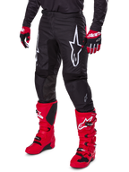 Alpinestars 2025 Fluid Haul bukser, motocross-bukser, sort, med et stort hvidt Alpinestars-logo, båret med stærkt røde støvler og røde og sorte handsker, holdbar 600D polyfabrik-konstruktion med ergonomisk snit til off-road kørsel