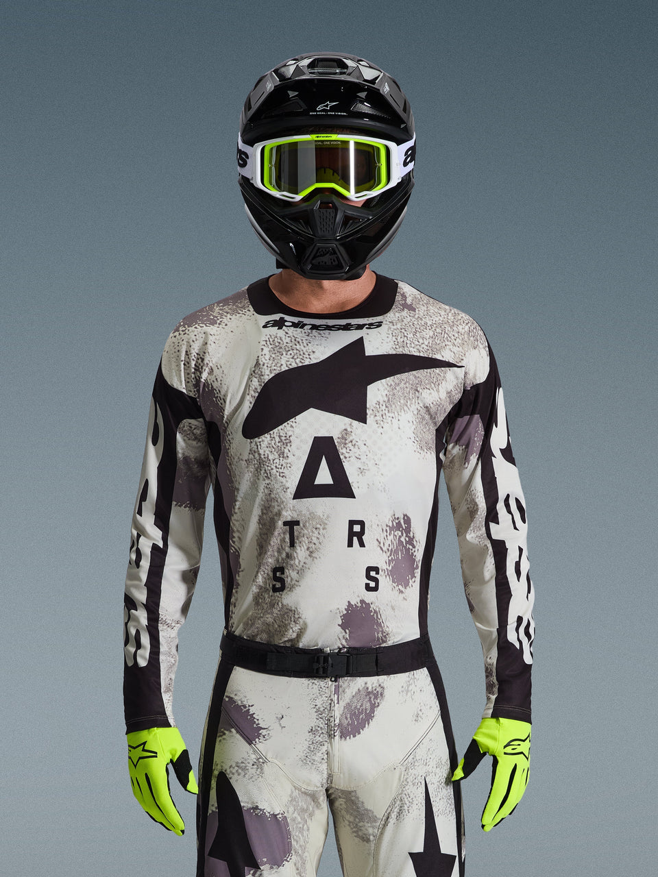 Motocross-kører iført Alpinestars 2026 Racer Lahnd Jersey, Sand Camo-mønster i grå og hvid, stort sort Astar-logo og branding på brystet, kombineret med en sort hjelm, neongule goggles og handsker, performance-udstyr til off-road kørsel