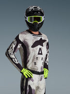 Motocross-kører iført Alpinestars 2026 Racer Lahnd-trøje og udstyrssæt i Sand Camo, lysegråt camouflage-mønster med sort logo-branding, sort hjelm med hvide og neongule goggles, lysende neongule handsker, professionelt off-road racerudstyr