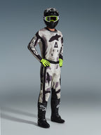 Motocross-kører iført 2026 Racer Lahnd-trøjen i Sand Camo, gråt og sort camouflagemønster med Alpinestars-branding, matchende motocross-bukser, neongule handsker, sort hjelm med gule goggles og sorte støvler, komplet professionelt off-road racerudstyr.