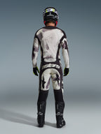 Motocrosskører iført komplet Alpinestars 2026 Racer Lahnd-udstyrssæt, set bagfra, Sand Camo-trøje og -bukser med lysegråt og sort abstrakt mønster, sort hjelm, sorte og neongule handsker og sorte støvler, med 'astars'-branding bag på bukserne