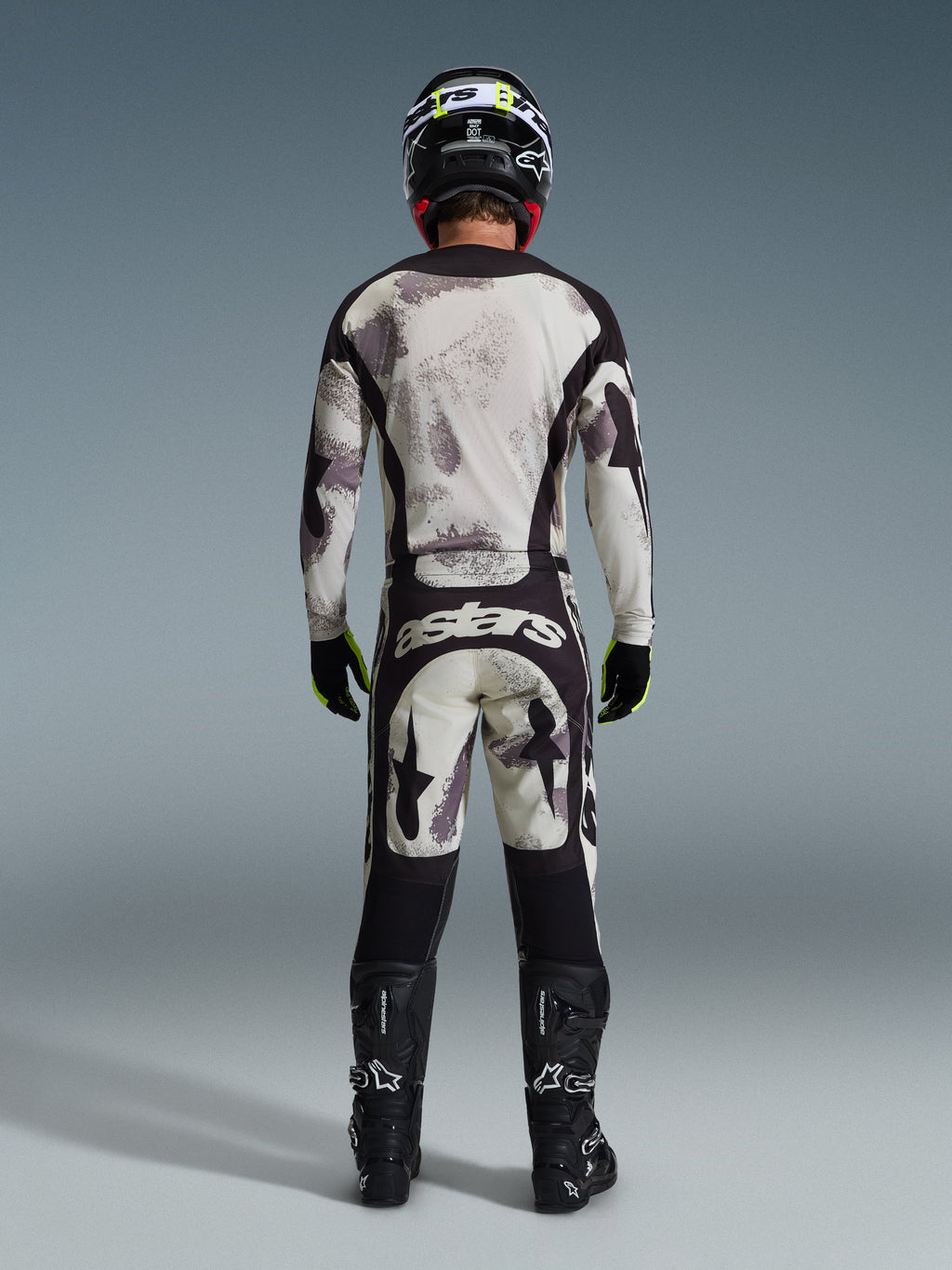 Motocrosskører set bagfra iført 2026 Racer Lahnd-trøje og matchende bukser i Sand Camo, med et abstrakt mønster i creme og grå samt sorte paneler, 'astars'-branding på bukserne, kombineret med sorte Alpinestars-støvler og en sort hjelm for et komplet off-road racing-look.