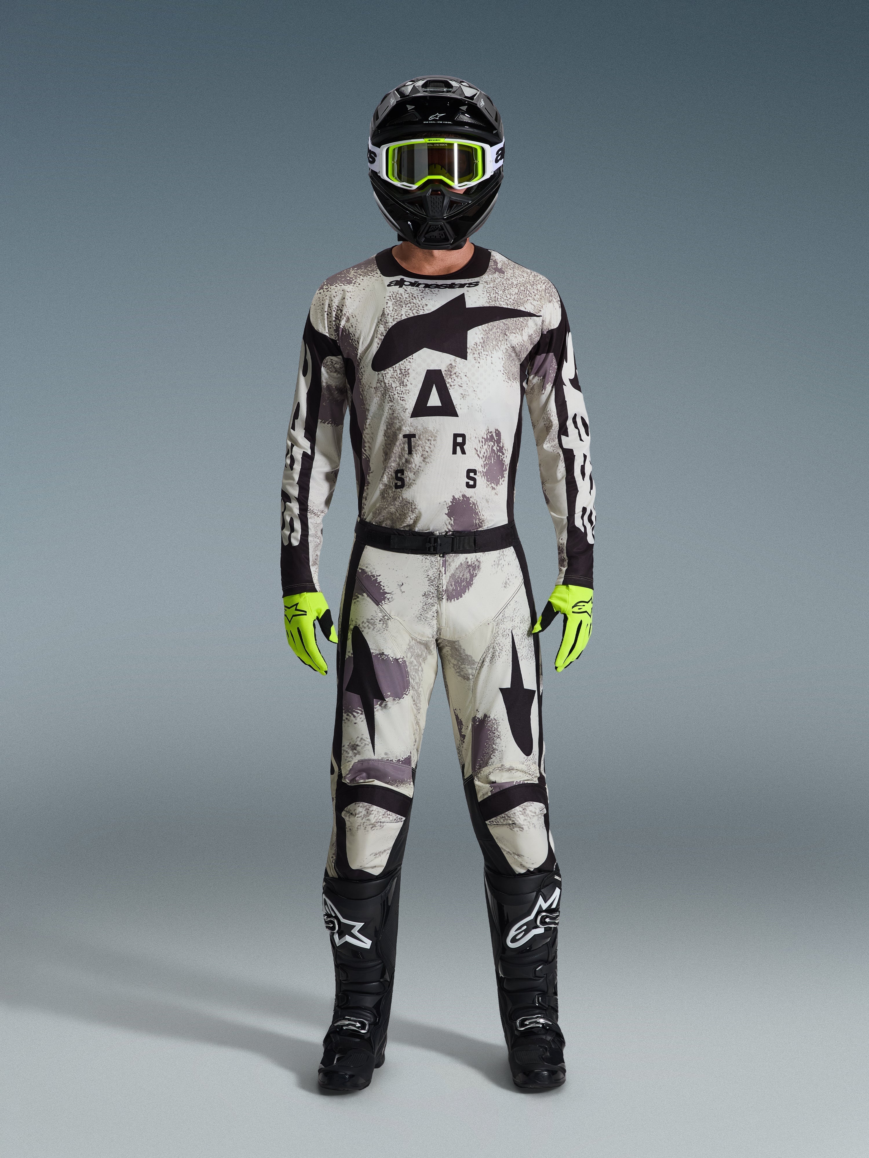 Motocross rider wearing 2026 Racer Lahnd Jersey and matching pants in Sand Camo, black helmet with neon yellow goggles, neon yellow gloves, and black boots, complete Alpinestars off-road racing gear set