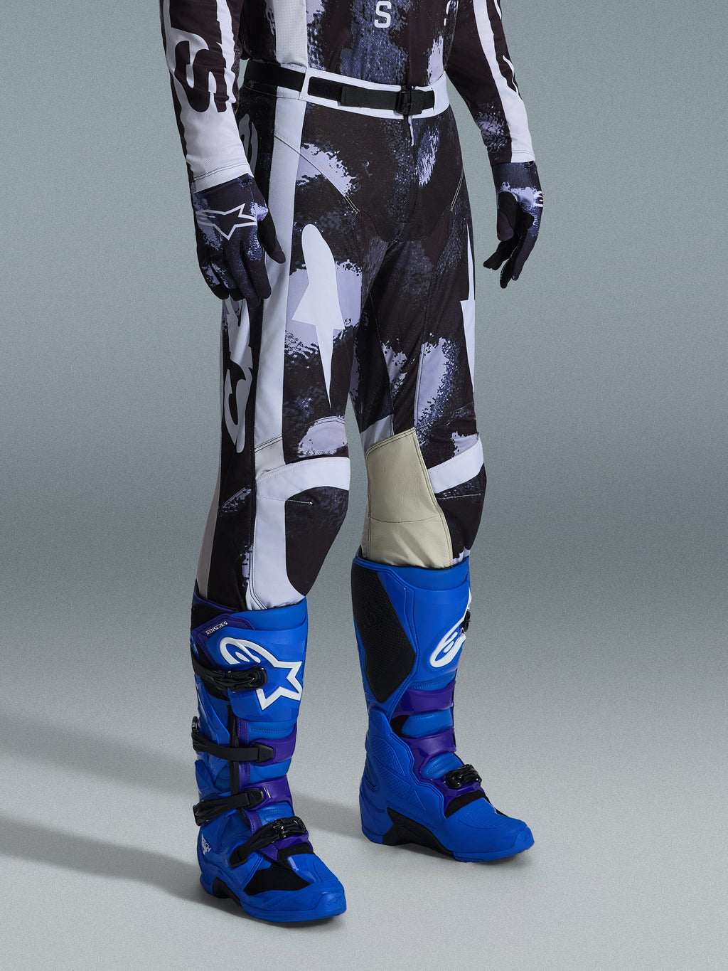 Alpinestars 2026 Racer Lahnd bukser, motocrossbukser, Iron Camo gråt og sort mønster, båret med klare blå racingstøvler og matchende handsker, med hvide paneler og gedelæder på indersiden af knæene, præstationsorienteret off-road udstyr