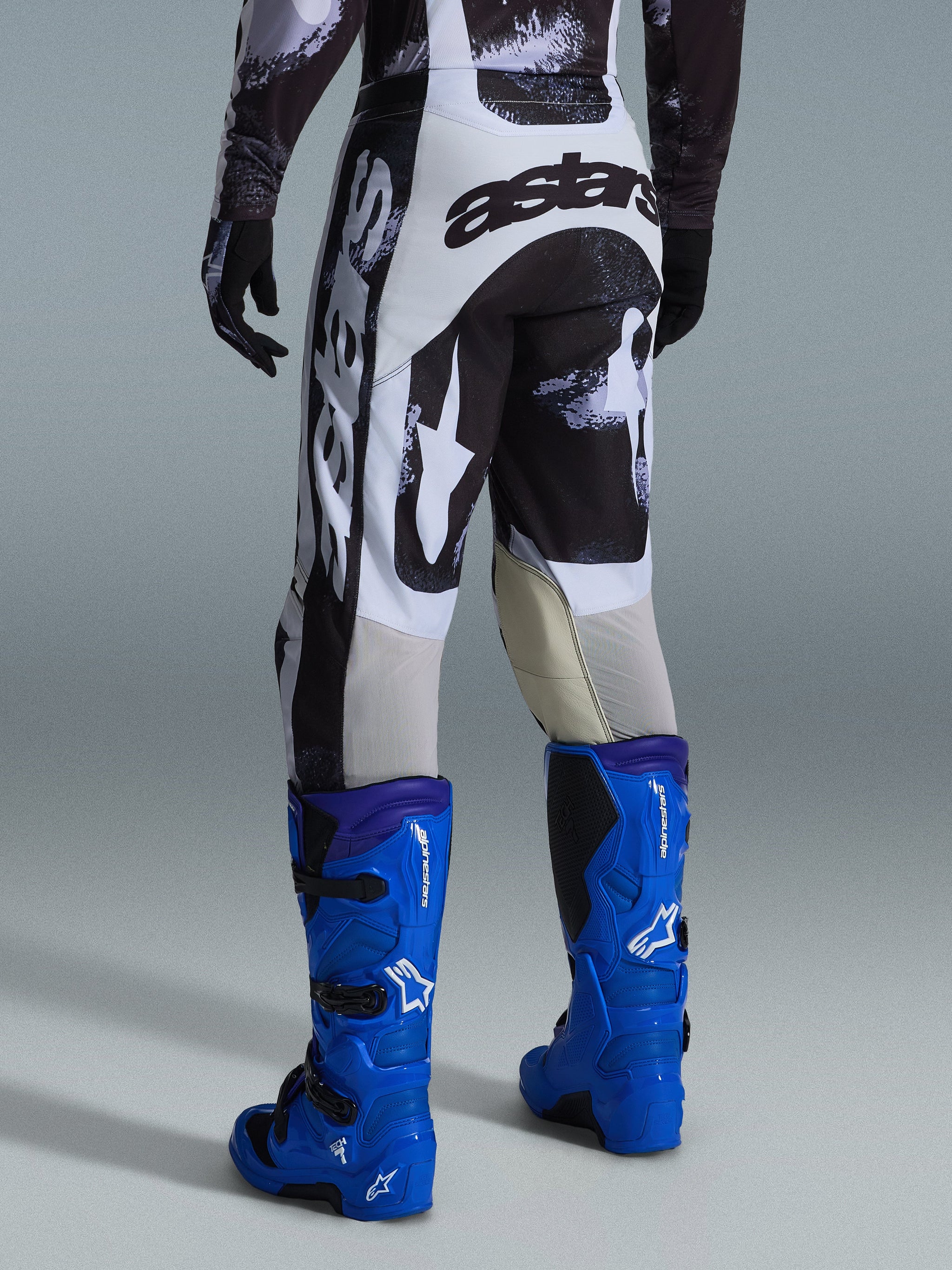 Alpinestars 2026 Racer Lahnd bukser, motocrossbukser, Iron Camo gråt og sort mønster, set bagfra med stort hvidt og sort astars-branding, kombineret med klare blå motocross-støvler, professionelt off-road racerudstyr
