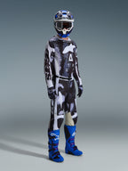 Motocross-rytter iført Alpinestars 2026 Racer Lahnd-trøje og matchende bukser i Iron Camo, med et sort og hvidt grafisk mønster, kombineret med blå støvler, en blå og hvid hjelm og sorte handsker, komplet racerudstyr til off-road kørsel.
