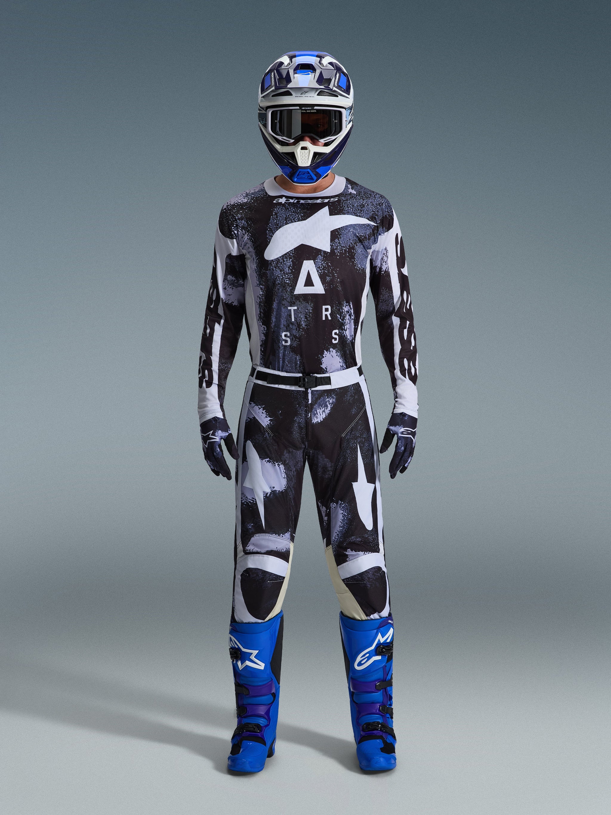 Motocross-kører iført Alpinestars 2026 Racer Lahnd bukser i Iron Camo, gråt og sort camouflage-design, matchende trøje, blå og hvid hjelm med goggles og lyseblå støvler, koordineret motocross-udstyrssæt.