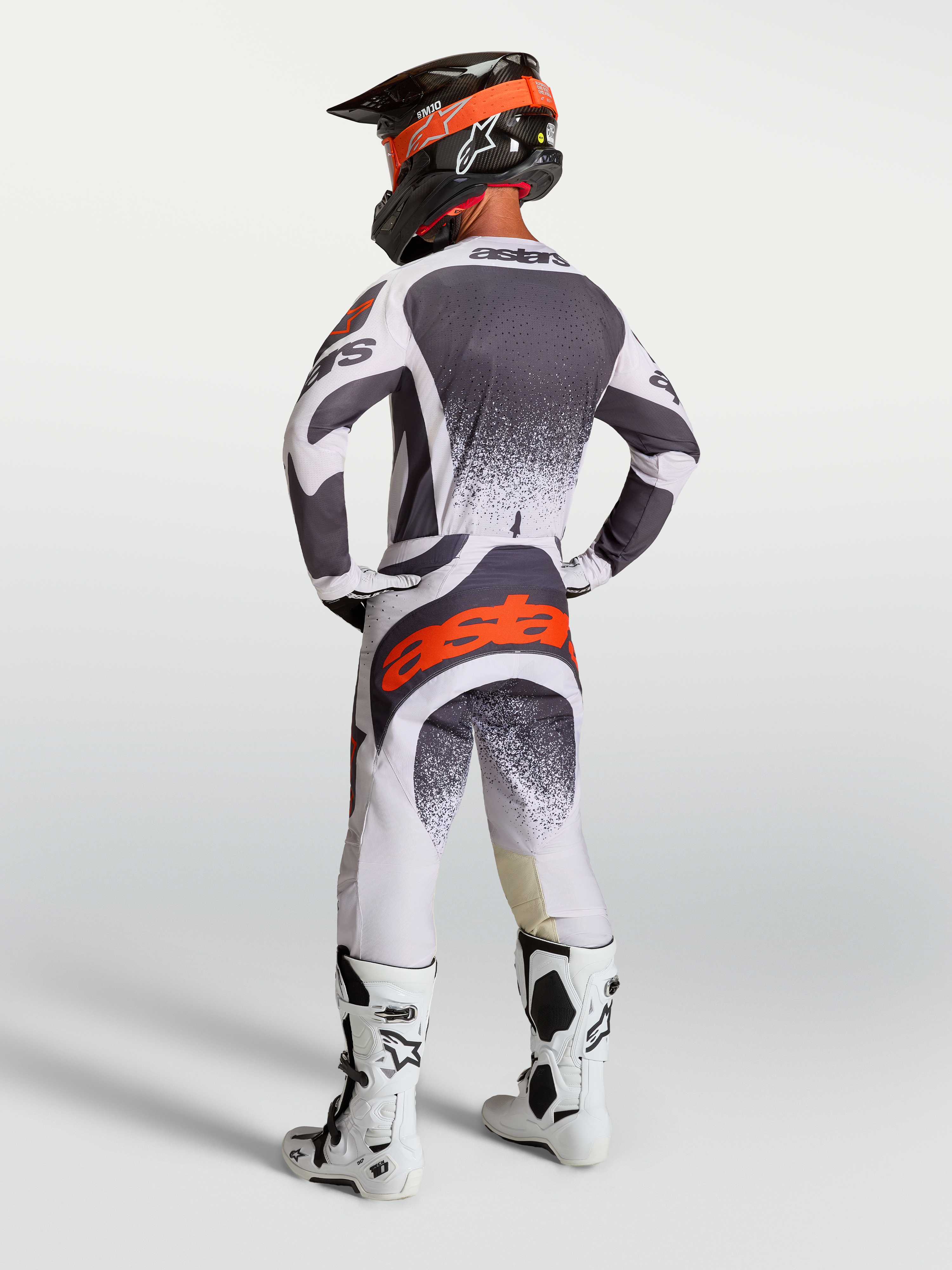 Alpinestars Techstar Swan Pants and Jersey, men's motocross gear in gray and white with red fluo accents, rear view on model.
