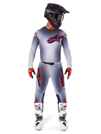 Motocross-kører iført Alpinestars 2025 Supertech Lipan bukser og matchende trøje i Grå Orange Fluo, med markante orange og navyblå logoer, kombineret med sort hjelm, røde handsker og hvide og sorte støvler, komplet racersæt til terrænkørsel.