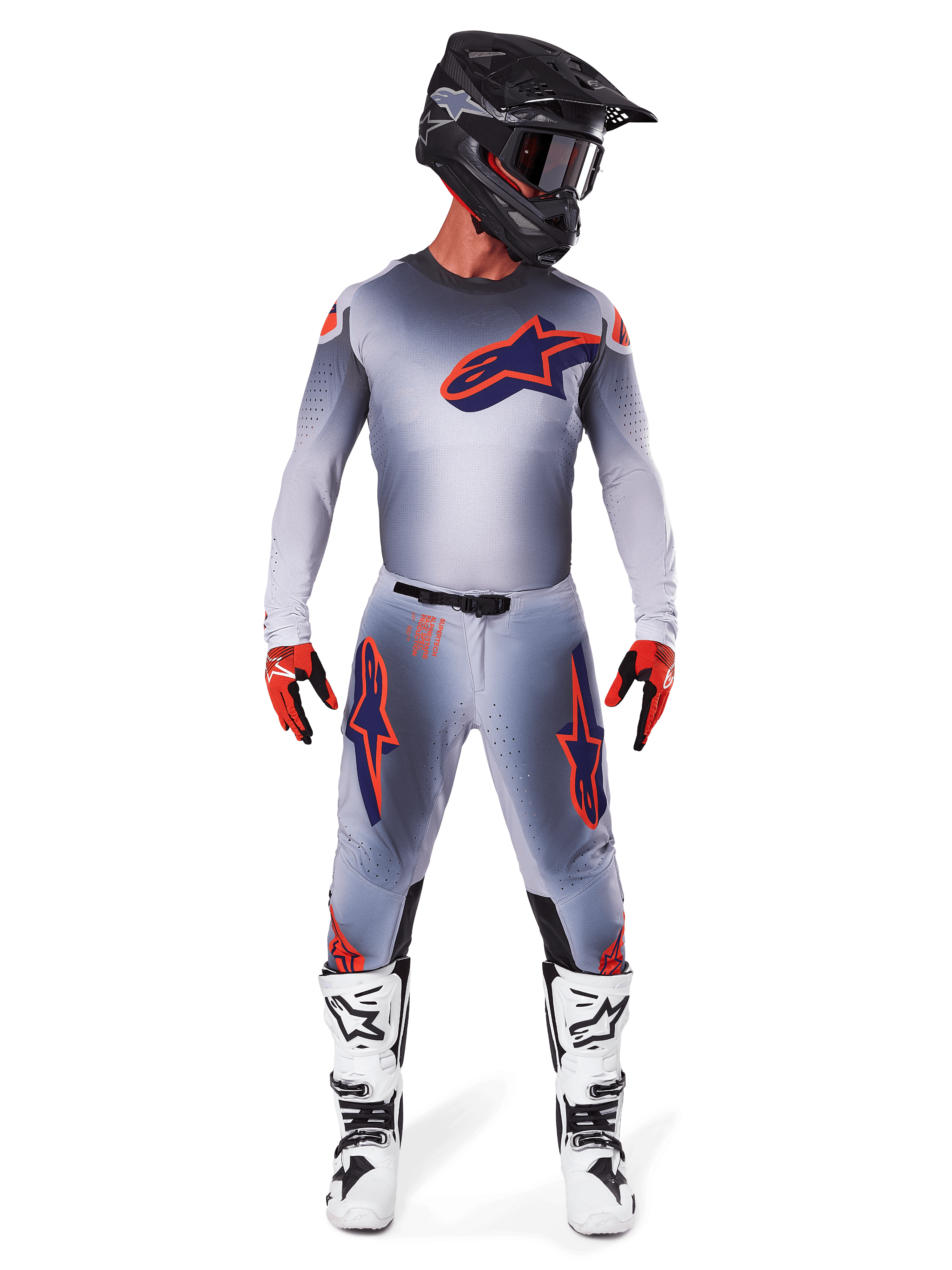 Motocross-kører iført Alpinestars 2025 Supertech Lipan bukser og matchende trøje i Grå Orange Fluo, med markante orange og navyblå logoer, kombineret med sort hjelm, røde handsker og hvide og sorte støvler, komplet racersæt til terrænkørsel.