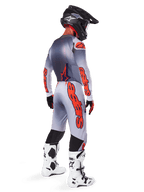 Motocrossrytter set bagfra iført Alpinestars 2025 Supertech Lipan-bukser i grå og fluoriserende orange, matchende langærmet trøje, sort hjelm og hvid-sorte tekniske støvler, komplet professionelt terrænracerudstyr.