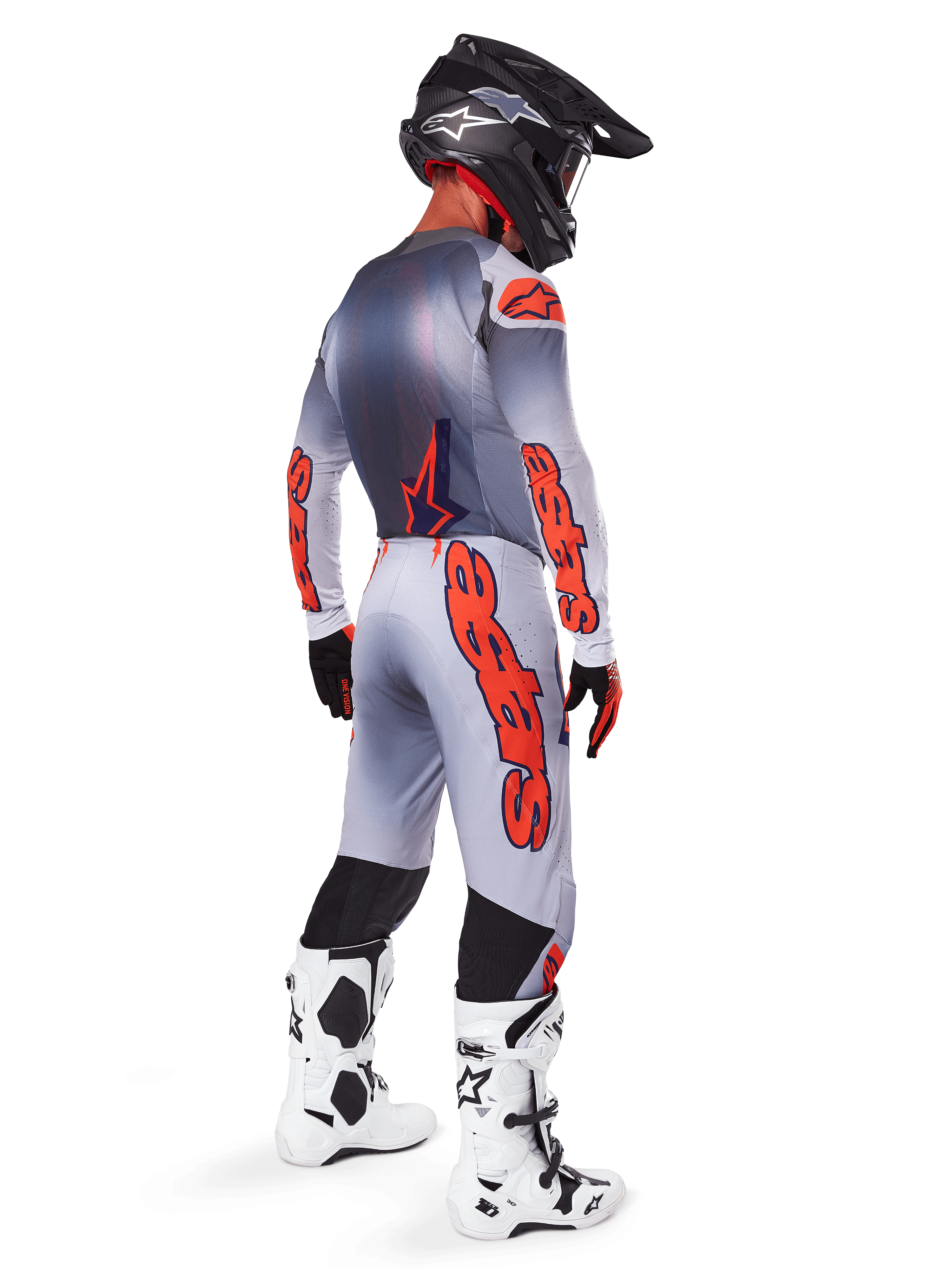 Motocrossrytter set bagfra iført Alpinestars 2025 Supertech Lipan-bukser i grå og fluoriserende orange, matchende langærmet trøje, sort hjelm og hvid-sorte tekniske støvler, komplet professionelt terrænracerudstyr.
