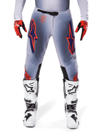 Alpinestars 2025 Supertech Lipan bukser, motocrossbukser, grå og orange fluo, bæres med røde og sorte handsker og hvide og sorte støvler, med store Alpinestars-stjernelogoer på lårene og ventilationsperforeringer til kørsel på professionelt niveau.