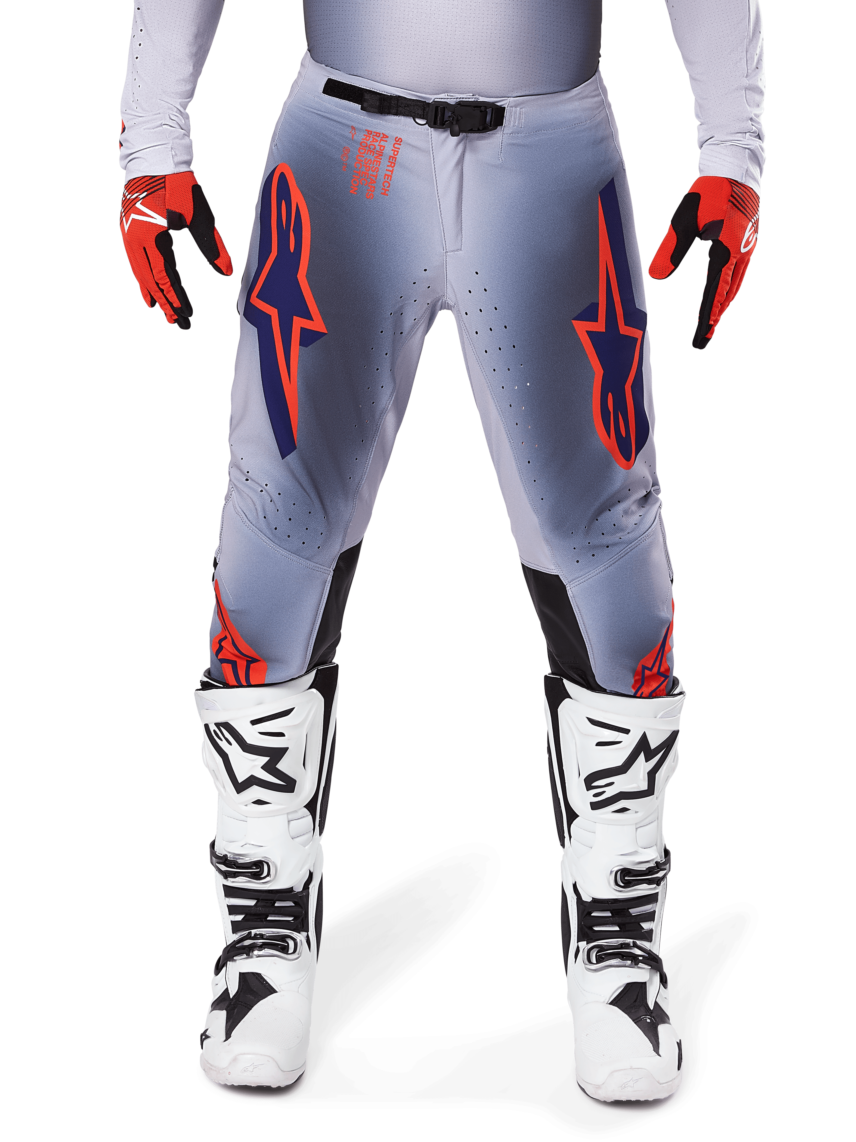 Alpinestars 2025 Supertech Lipan bukser, motocrossbukser, grå og orange fluo, bæres med røde og sorte handsker og hvide og sorte støvler, med store Alpinestars-stjernelogoer på lårene og ventilationsperforeringer til kørsel på professionelt niveau.