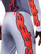 Alpinestars 2025 Supertech Lipan bukser og jersey, motocross-udstyrssæt, grå og fluoriserende orange, nærbillede af siden og bagsiden, der viser stort orange Alpinestars-branding, performance rip-stop-stof med perforeret ventilation