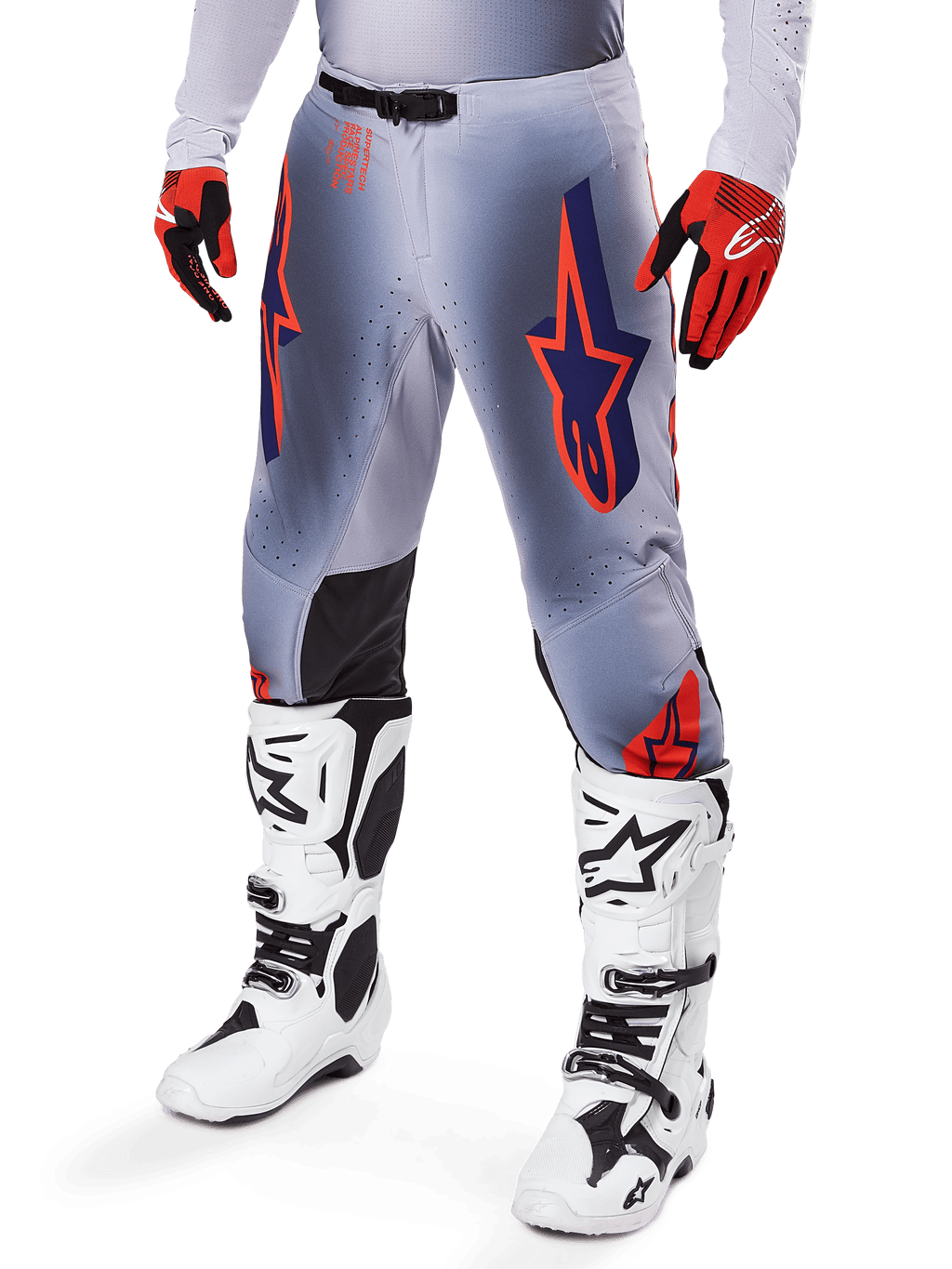 Alpinestars 2025 Supertech Lipan bukser, motocross-bukser, grå og orange fluo, med mørkeblå stjernedesigns og sorte indvendige knæpaneler, båret med rød-orange handsker og hvide støvler, professionelt udstyr til terrænkørsel