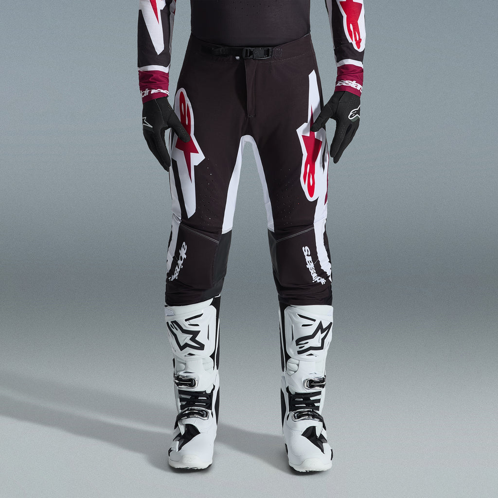 Alpinestars 2026 Supertech AFD Vista Gear Set, motocrosskører iført sorte bukser med store hvide og røde logoer, matchende performance jersey med bordeauxrøde manchetter, sorte handsker og hvide professionelle racingstøvler, højtydende off-road racingoutfit