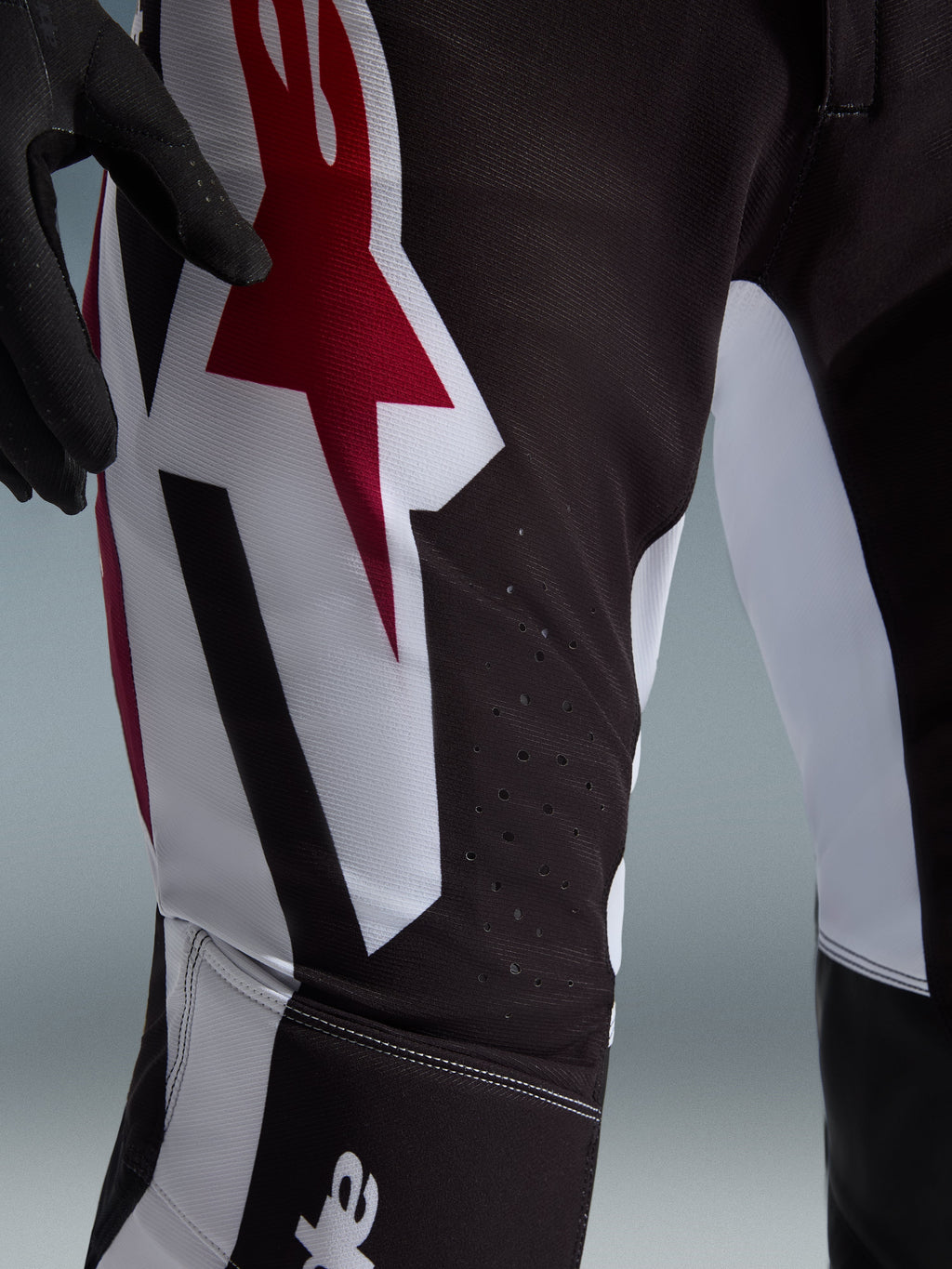 Alpinestars 2026 Supertech AFD Vista bukser, motocross-bukser, sort, rød og hvid, nærbillede af låret med et stort rødt og hvidt Astars-logo og laserskårne perforationer til ventilation.