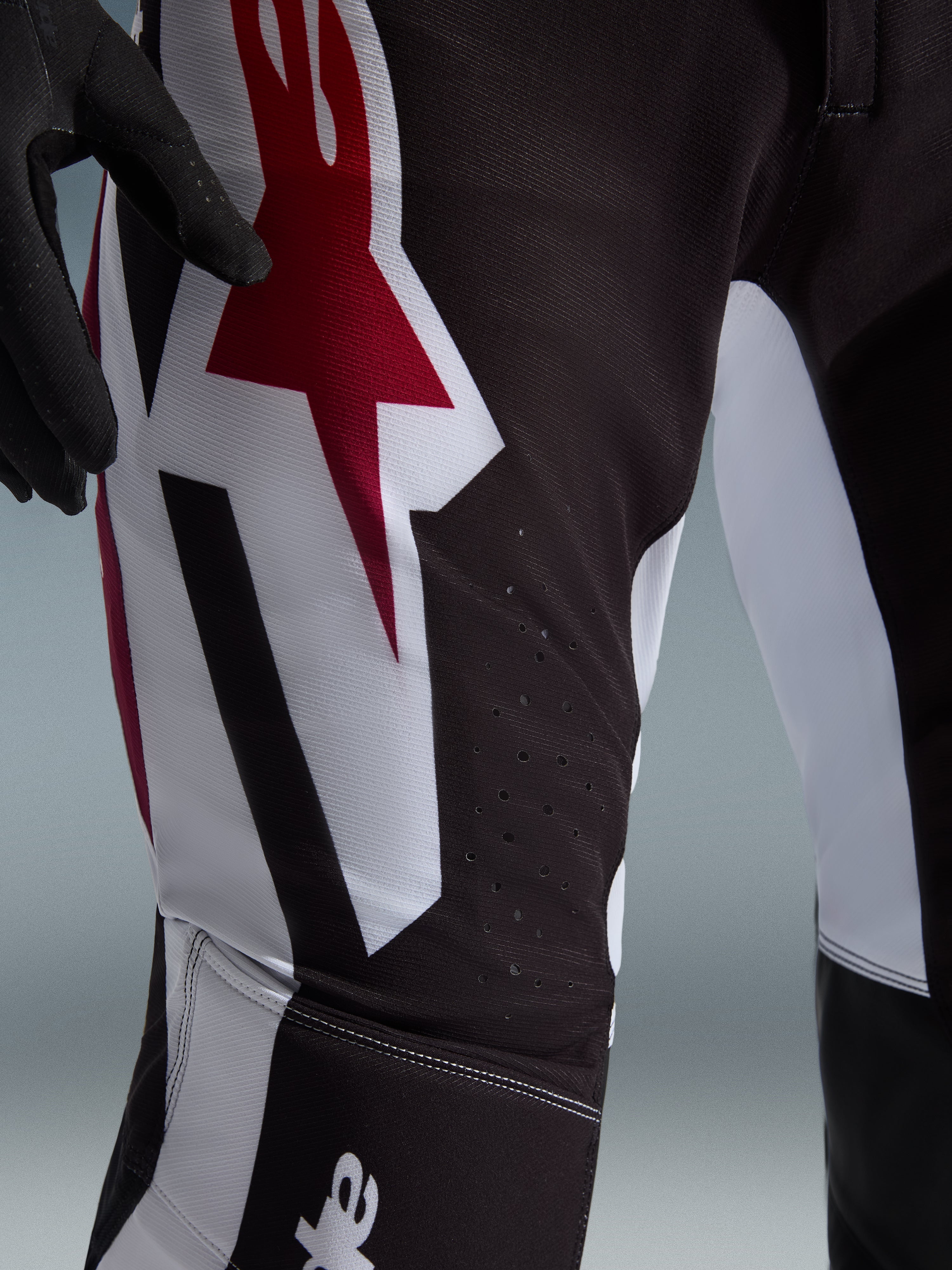 Alpinestars 2026 Supertech AFD Vista bukser, motocross-bukser, sort, rød og hvid, nærbillede af låret med et stort rødt og hvidt Astars-logo og laserskårne perforationer til ventilation.
