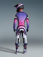 Motocrosskører set bagfra iført komplet racerudstyr, lilla og pink trøje med gradient, Alpinestars 2026 Supertech AFD Vista bukser i hvid, lilla og sort, sort hjelm med lilla goggles, hvide og lilla støvler, koordineret off-road racersæt.