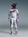 Motocross-kører iført Alpinestars 2026 Supertech AFD Vista Gear Set, hvid trøje og bukser med pink og lilla gradient stjerne-grafik, sort hjelm med matchende goggles, hvide støvler med pink detaljer og hvide handsker, koordineret professionelt off-road racerudstyr